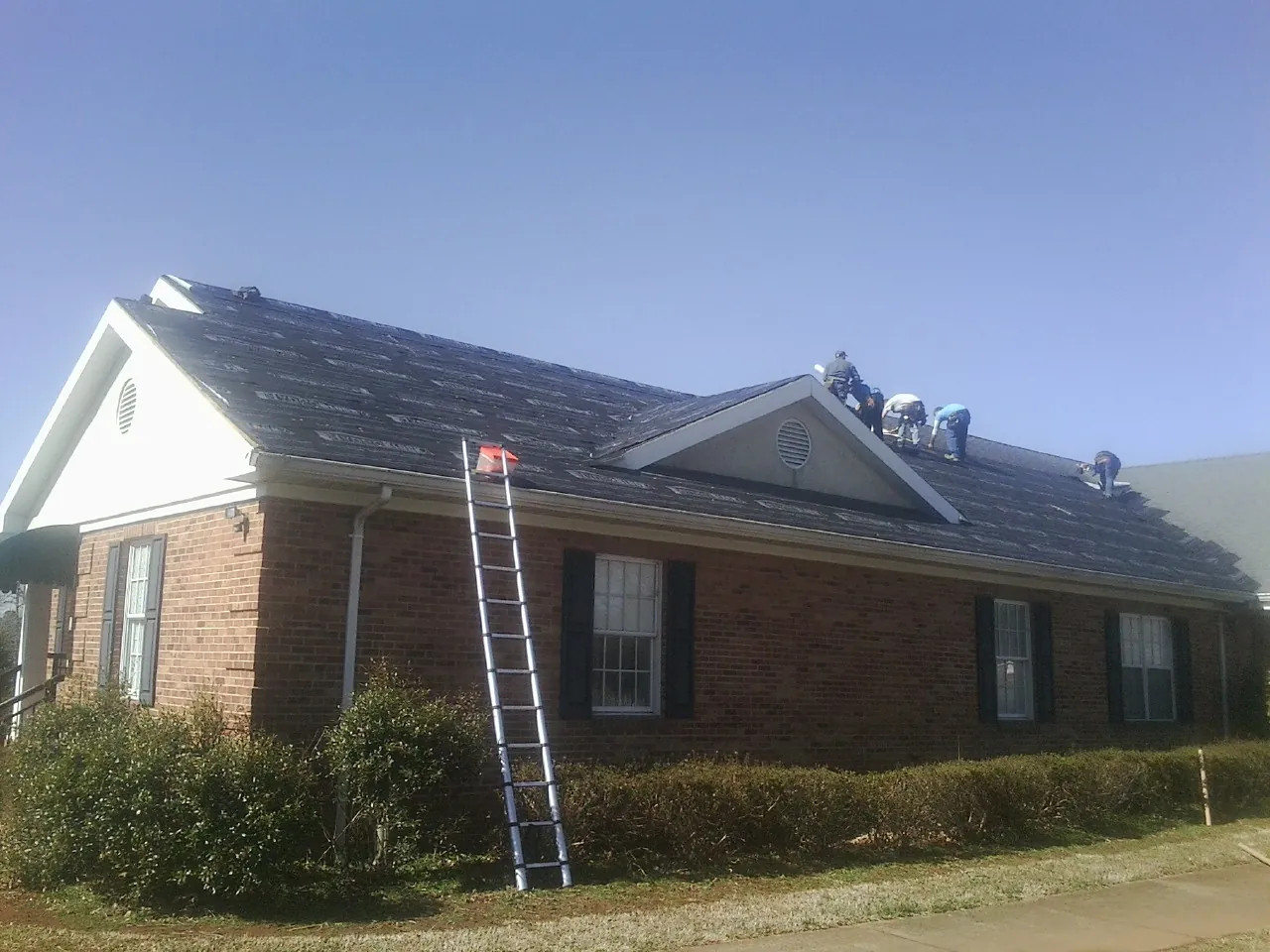 Crew tearing shingles off a brick ranch roof with a ladder set — Metal Roof Repair work by our crew in State College