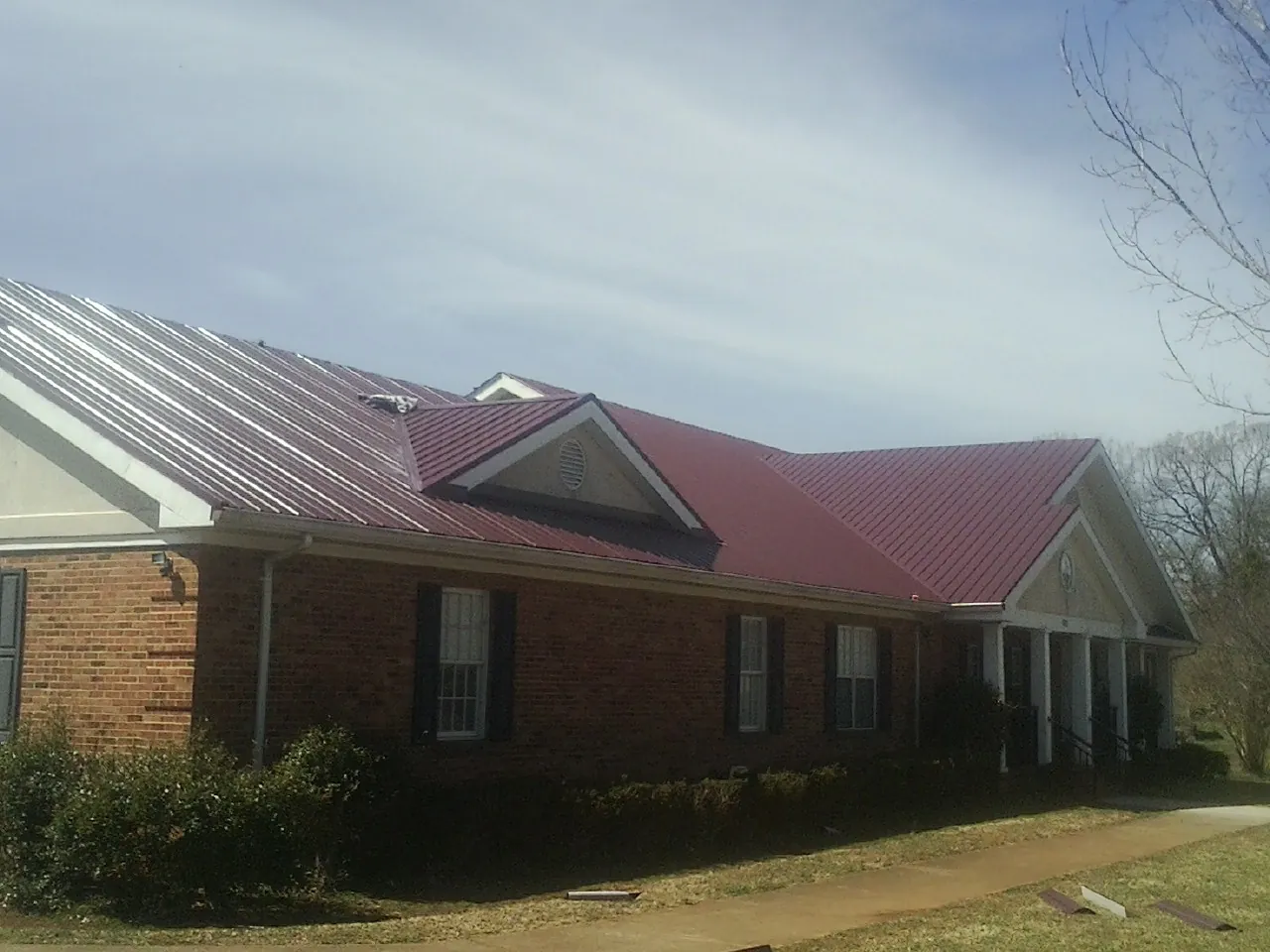 Red metal roof with gabled entries on a long brick building, from a Hail Damage Roof Repair job in State College