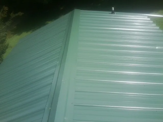 New green metal panels meeting at the ridge of a roof — Flat Roof Repair work by our crew in State College