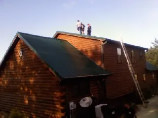 Crew on the ridge of a green metal roof on a two story log home in State College