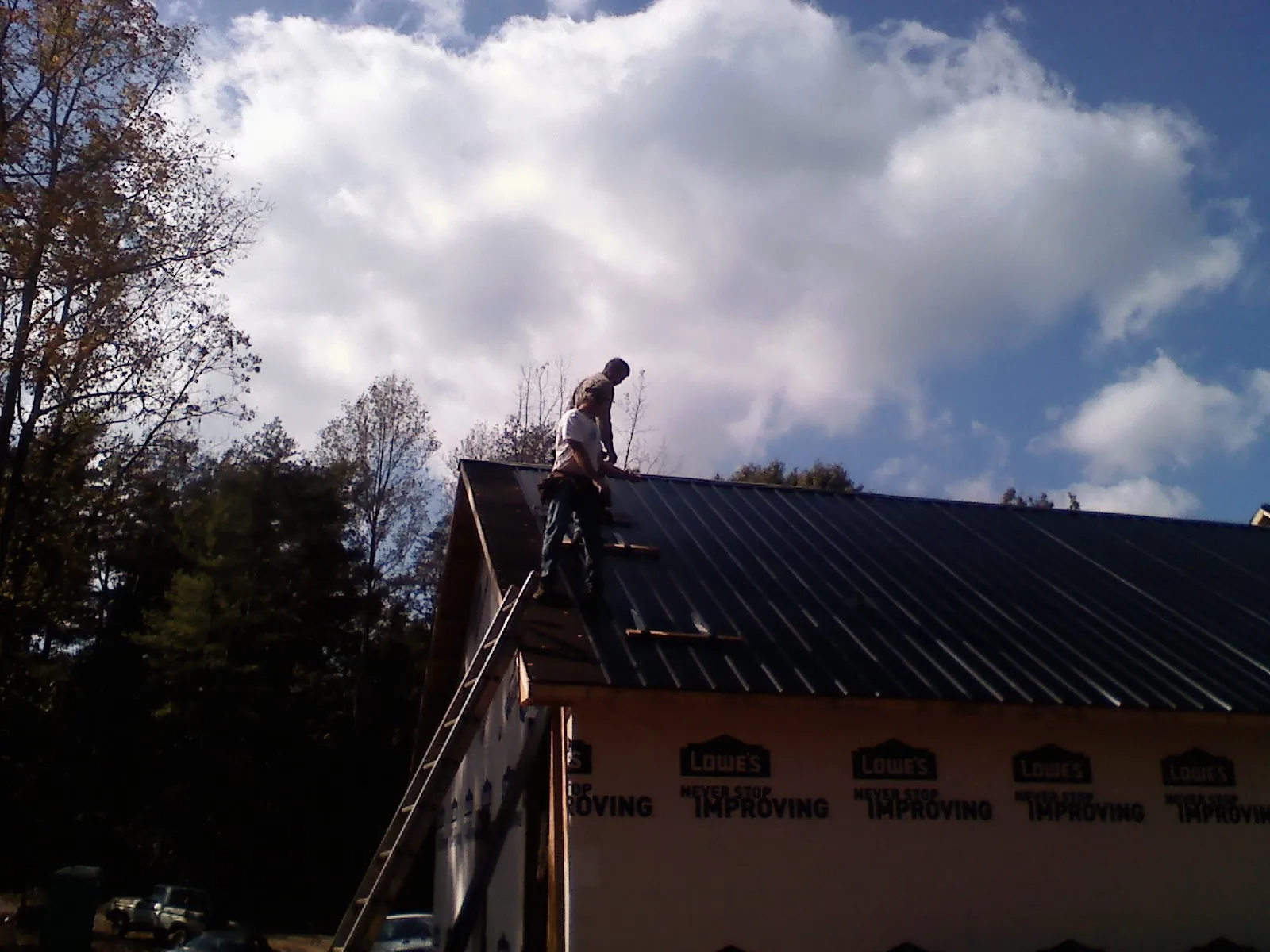 Roofer fastening dark metal panels high against a cloudy sky, from a Roof Inspection job in State College