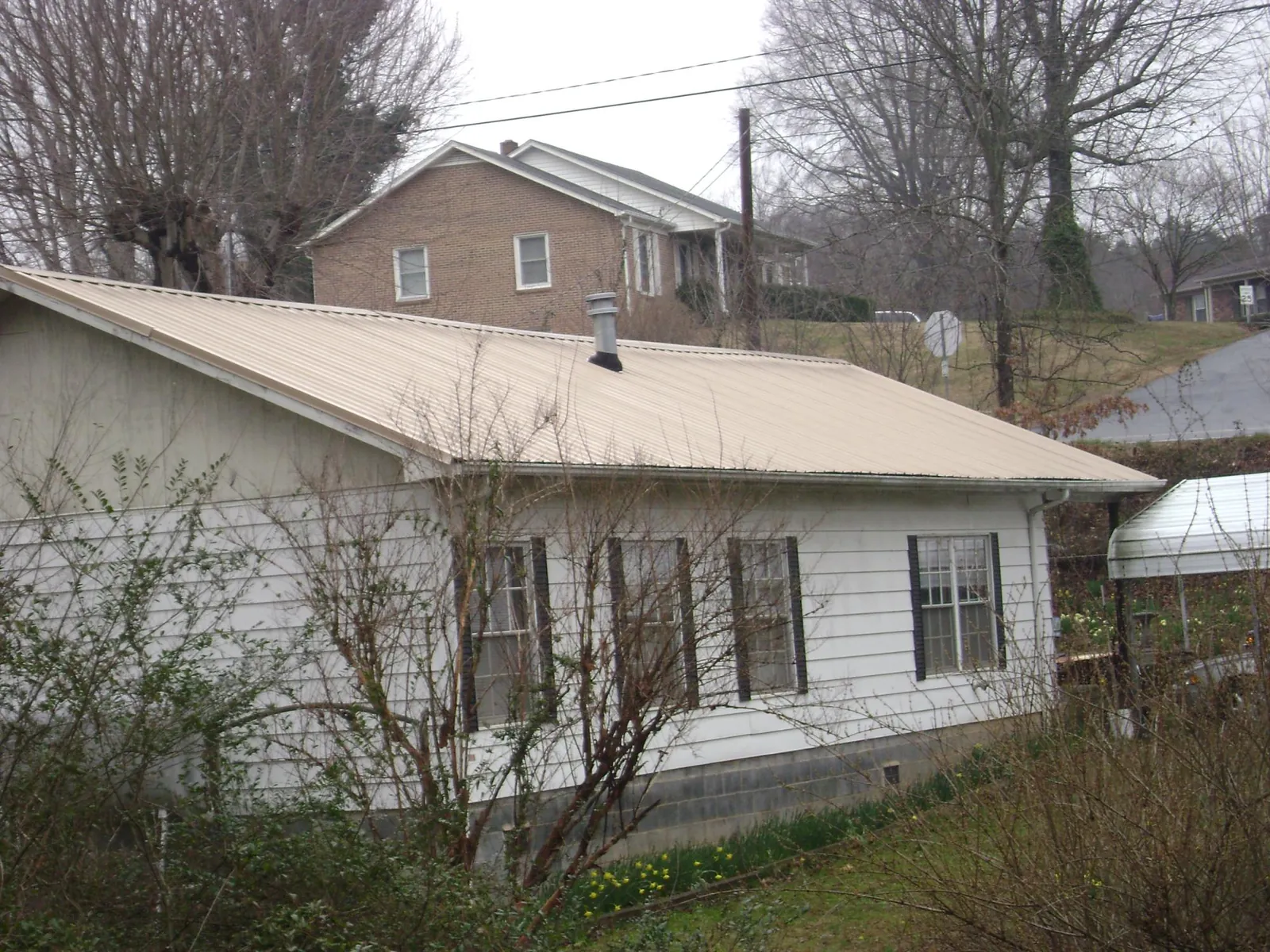 Tan metal roof on a white sided house set into a hillside — Commercial Roofing by Roofing Brothers in State College